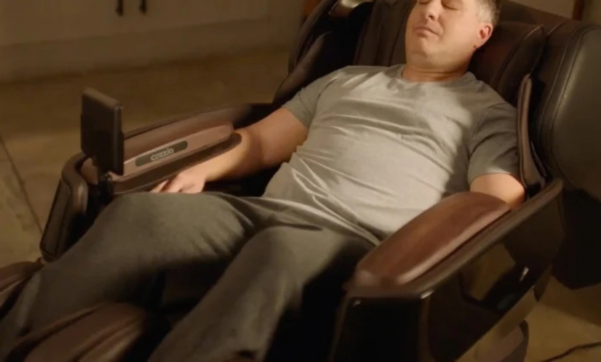 A man reclining in a brown massage chair in a dimly lit indoor setting.