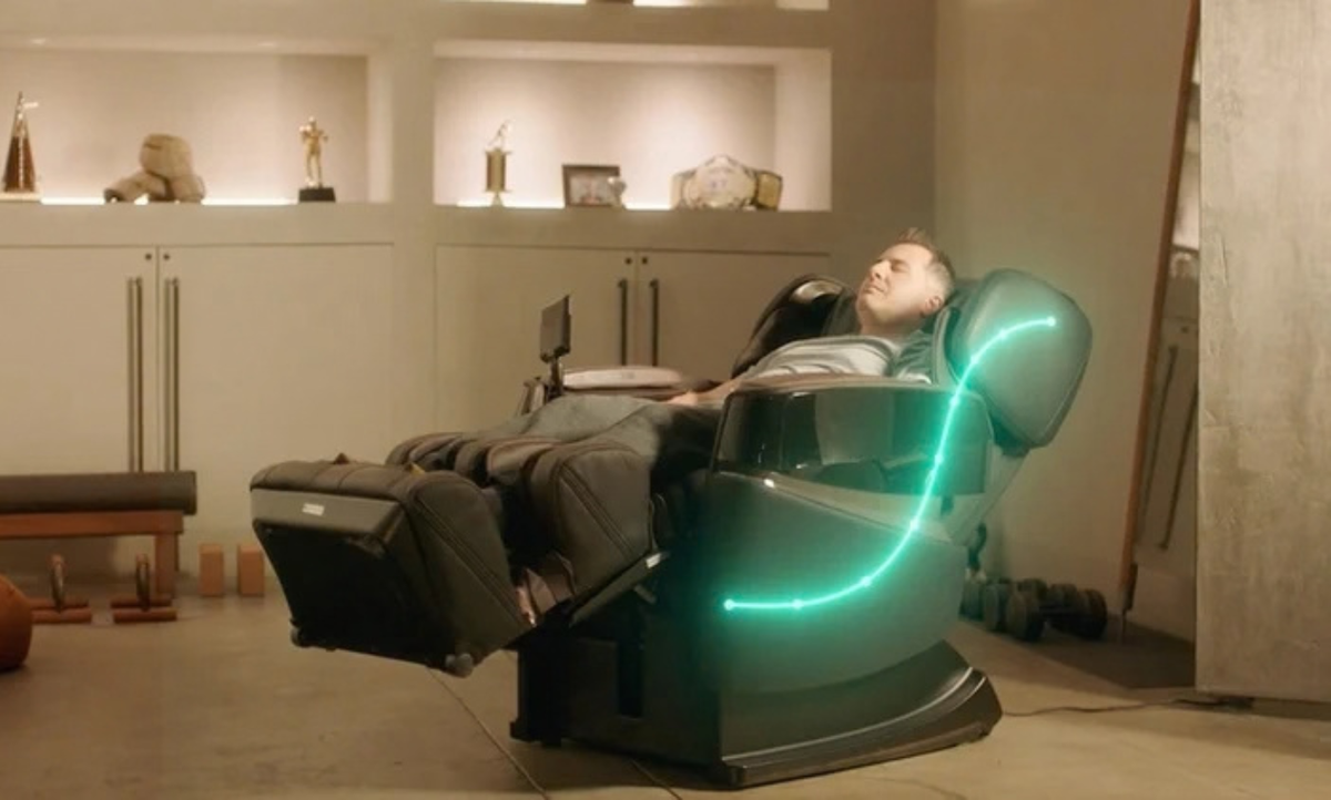 A person reclining in a dark massage chair with glowing green light accents in a modern indoor room.